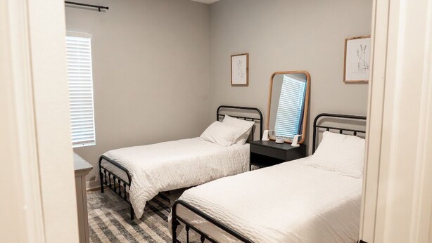 A bedroom with two single beds, a nightstand, a mirror, and a window with blinds.