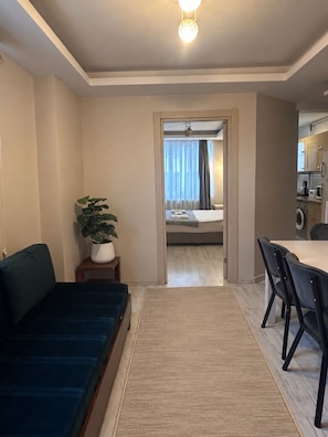 A modern hotel room with a sofa, a dining table with chairs, a potted plant, and a view into the adjacent bedroom. - Taksim cozy apartments (Istanbul)