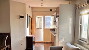 A living room with a sofa, a wooden floor, a patterned rug, a kitchen area with a refrigerator, and a window with curtains. - Taksim cozy apartments (Istanbul)