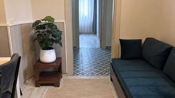 A compact living space with a sofa, a small table, a chair, a potted plant, and a tiled floor.