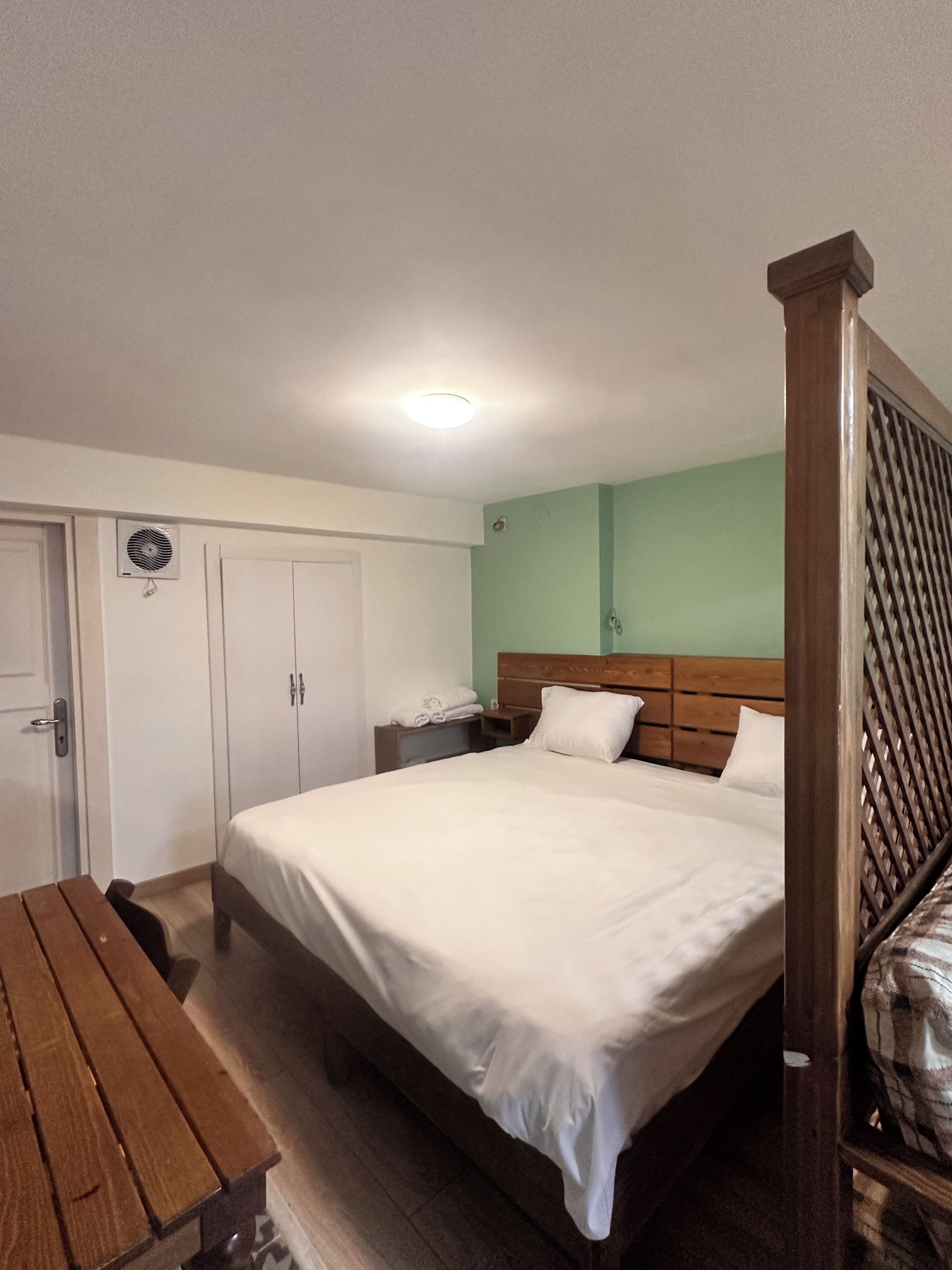 A hotel room with a bed, a wooden headboard, a bedside table, a desk, and a wardrobe.