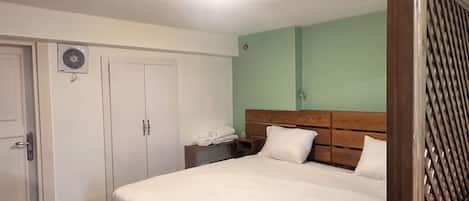 A hotel room with a bed, a wooden headboard, a bedside table, a desk, and a wardrobe.