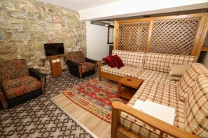 A living room with a stone wall, a television on a stand, a sofa, two armchairs, and a patterned rug. - Taksim cozy apartments (Istanbul)