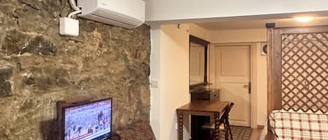 Un salon avec un mur en pierre, un téléviseur, une table à manger en bois et un canapé à carreaux.