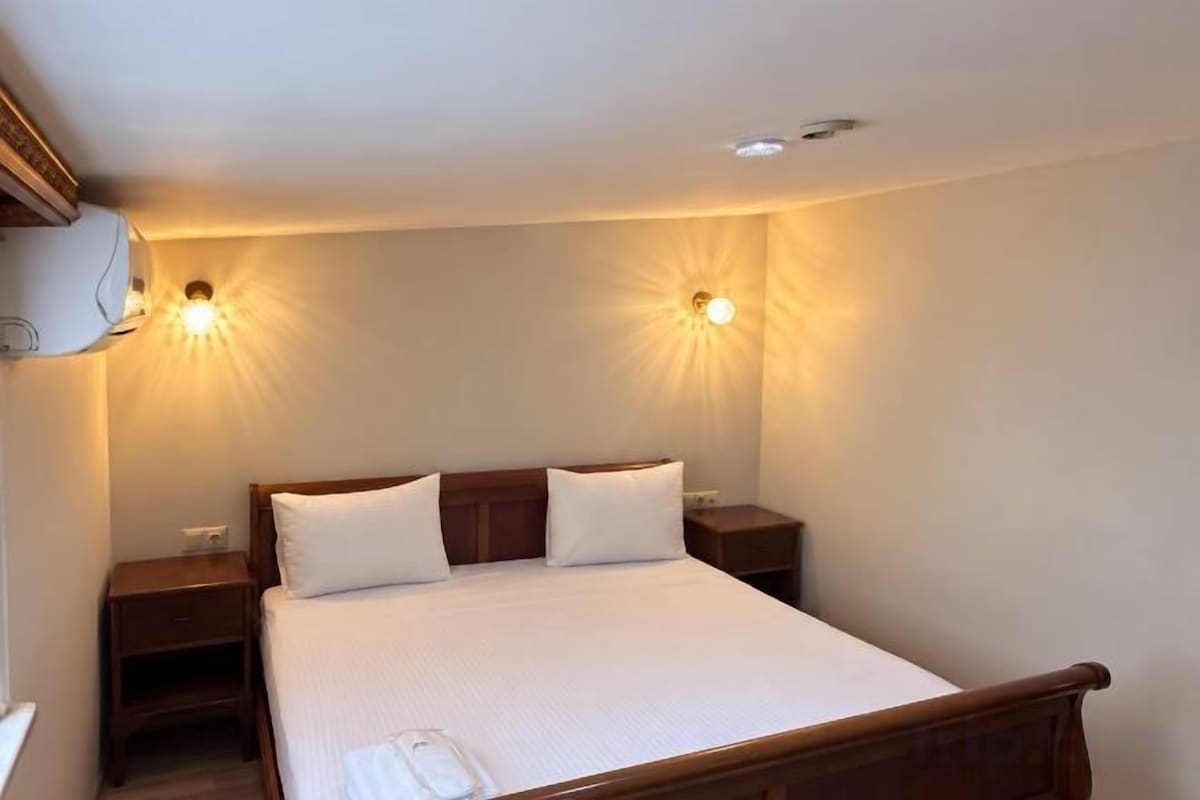 A neatly made bed with a wooden headboard, two bedside tables, and wall-mounted lights.