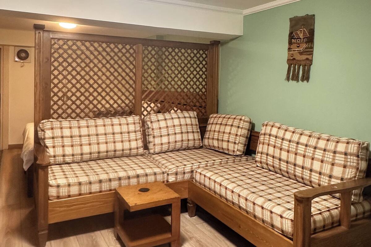 Een woonkamer met een houten hoekbank, een kleine houten tafel en een decoratieve wandversiering.