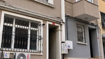 Un immeuble à plusieurs étages doté de balcons, avec un appareil de climatisation visible, et une rue bordée de bollards.