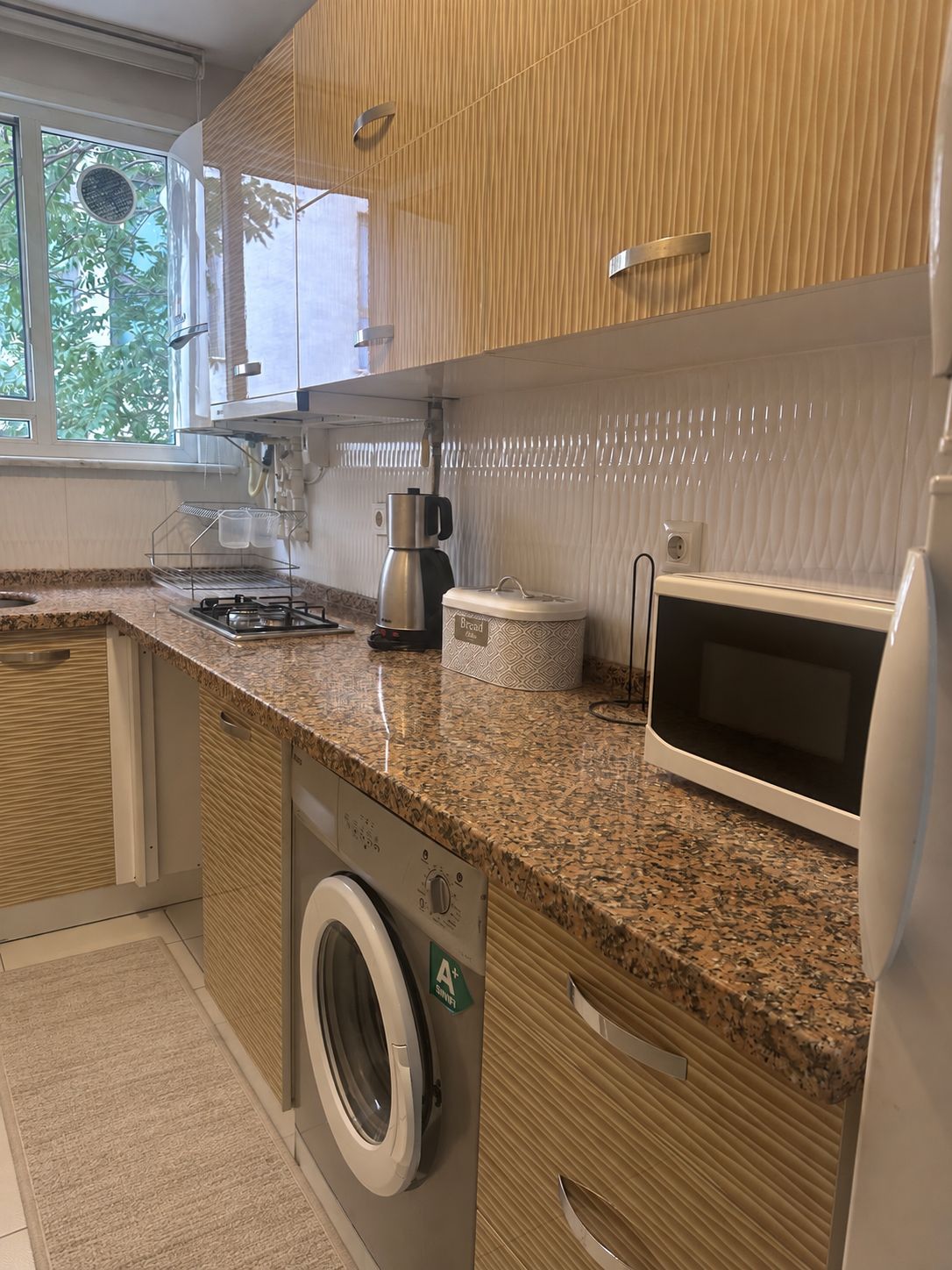 Una cocina moderna con lavadora integrada, cafetera y microondas.