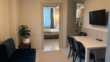 A hotel room with a bed, a desk, a TV, and a plant.