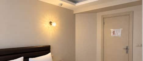 A hotel room with a large bed, bedside tables, a wardrobe, and a ceiling light fixture.