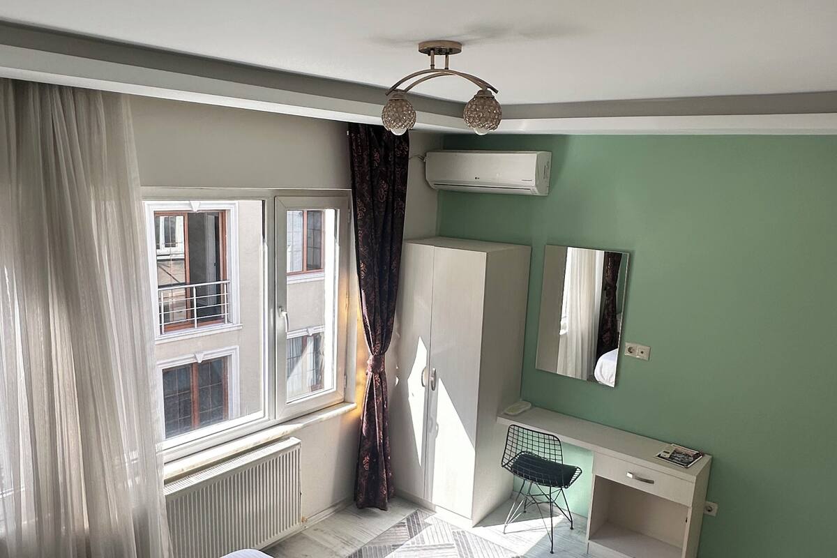 Een slaapkamer met een bed, een bureau, een spiegel en een raam met gordijnen.