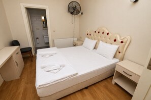 A neatly made bed with white linens, a bedside table, a nightstand, a wall-mounted fan, and a door leading to a bathroom. - Taksim cozy apartments (Istanbul)