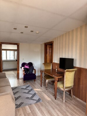 A living room with a wooden dining table, two chairs, a sofa, and a television.