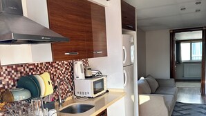 A modern kitchen with wooden cabinets, a microwave, and a built-in oven. There is a dining area with a sofa and a view of the outdoors. - Taksim cozy apartments (Istanbul)