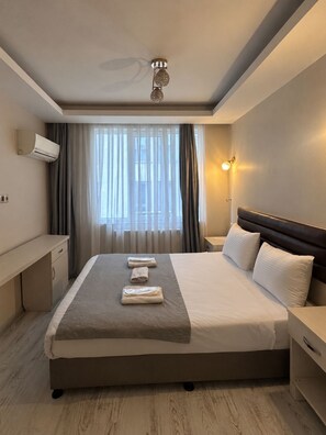A hotel room with a bed, bedside tables, a nightstand, a wall-mounted air conditioner, a ceiling fan, and a window with curtains. - Taksim cozy apartments (Istanbul)