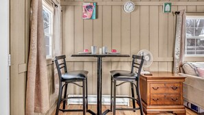 Una habitación con un revestimiento de madera en la pared, una mesa con dos sillas, una mesita de noche de madera y un reloj.