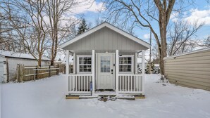 Una pequeña cabaña de madera de un solo piso con un porche delantero, rodeada de nieve y árboles desprovistos de hojas.