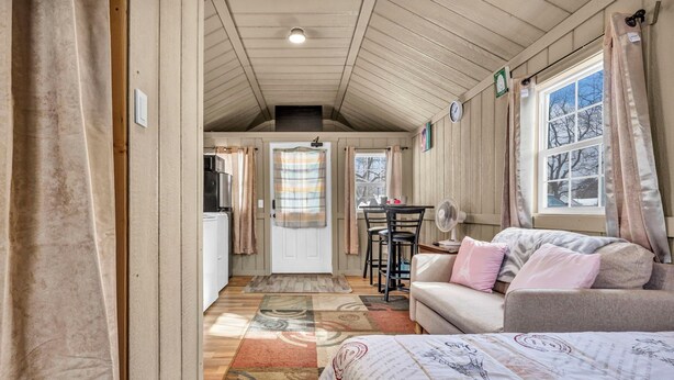 Una habitación acogedora con cama, sofá, mesa de comedor con sillas, ventilador y ventana con cortinas.