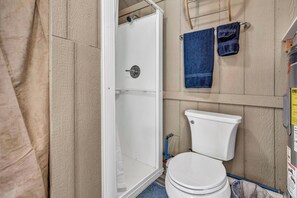 Une salle de bain avec des toilettes blanches, un espace douche et des murs en bois.