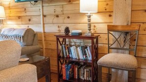 A cozy cabin interior with wooden walls, a bookshelf, a television, and two chairs. - Pinhoti Ridge Retreat Cabin 1, Pinhoti Path (Talladega)