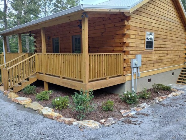 A log cabin with a wooden porch and a small set of stairs leading up to it.
