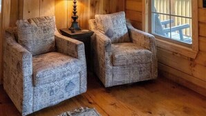 A cozy cabin interior with wooden walls, two patterned armchairs, a table with a lamp, and a painting on the wall. - Pinhoti Ridge Retreat Cabin 1, Pinhoti Path (Talladega)