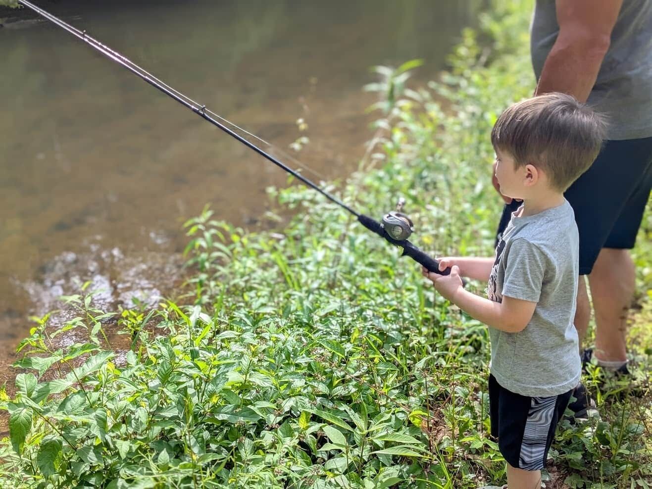 A child fishing by a calm water body with lush greenery around.