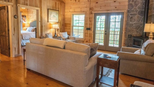 A cozy log cabin interior with a large sofa, a smaller armchair, a fireplace, and a stone wall. - Pinhoti Ridge Retreat Cabin 1, Pinhoti Path (Talladega)