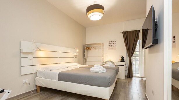 A bedroom with a bed, bedside tables, a TV, and a window with curtains.
