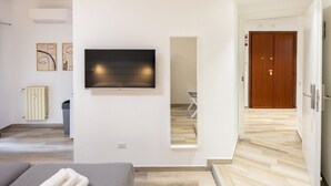 A modern hotel room with a flat-screen TV, a wooden door, and a view of the hallway.