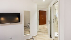 A hallway with a flat-screen TV mounted on the wall, a wooden door, and a glass shower area.