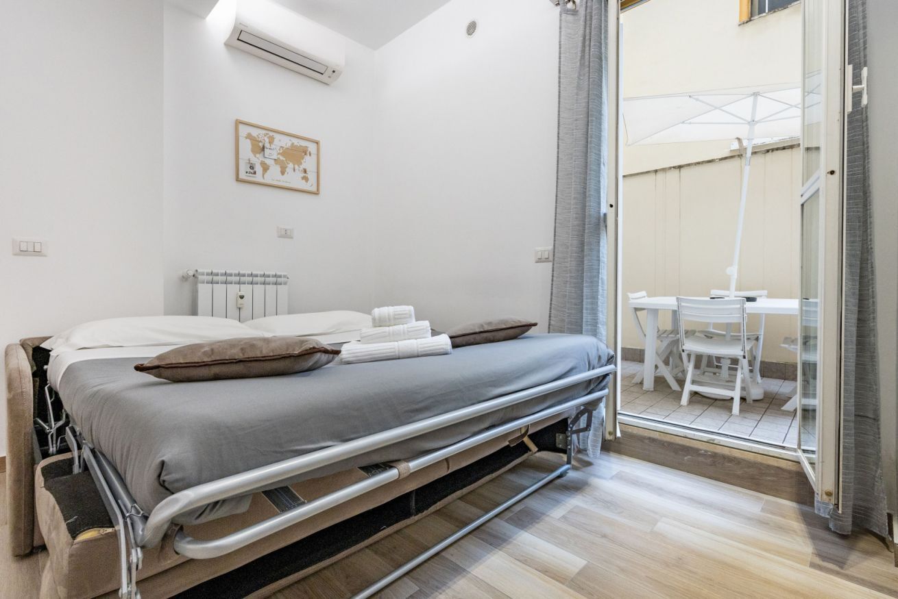 Ein modernes Schlafzimmer mit Bett, Heizkörper, einer Weltkarte an der Wand und Blick auf einen Außenbereich mit Tisch und Stühlen.