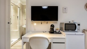 A small, modern room with a white desk, a flat-screen TV mounted above it, a microwave, and a small kitchenette area.