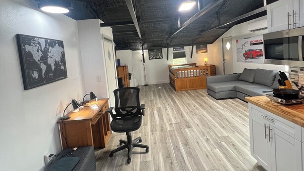 Un espacio de oficina moderno con un escritorio de madera, una silla de oficina y un sofá. Hay una zona de cocina con microondas y cocina.