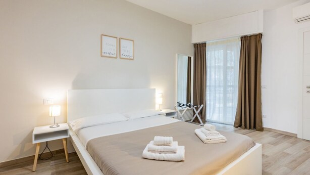 Habitación de hotel moderna con una cama grande, mesitas de noche con lámparas, un escritorio y vistas al exterior.