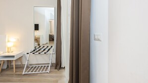 Una habitación de hotel con una cama, un escritorio con lámpara, un espejo y una ventana con cortinas.
