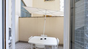 Un juego de mesa y sillas blancos bajo un paraguas blanco en un patio con baldosas.