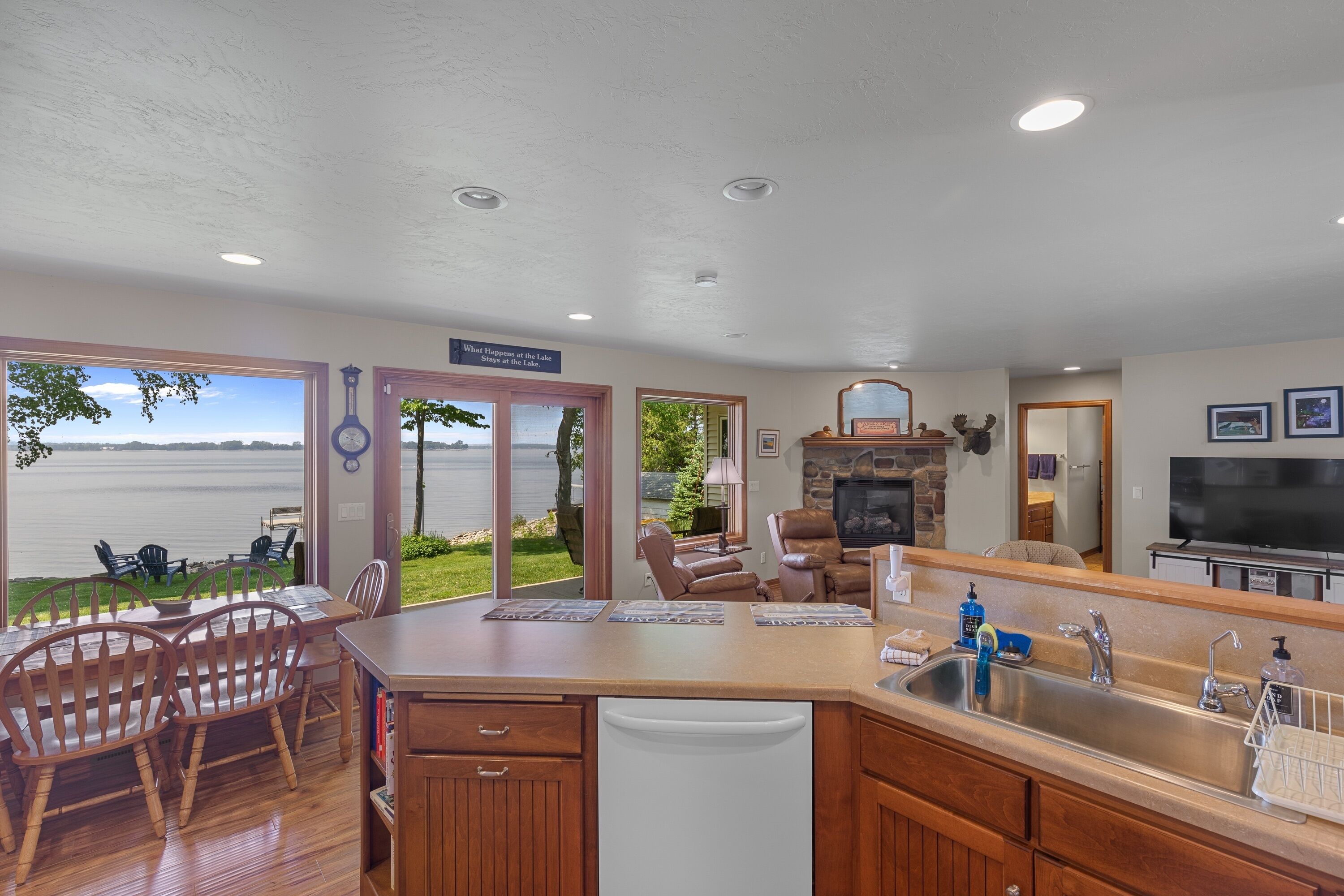 A spacious kitchen with a large island, a dining area with wooden chairs, a fireplace, and a view of the lake.