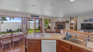 A spacious kitchen with a large island, a dining area with wooden chairs, a fireplace, and a view of the lake. - Relaxing Lakefront Cottage, Kayaks, Bikes, Fishing (Sturgeon Bay)