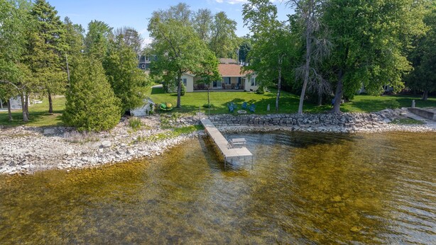 A riverside property with a dock, stone walls, and a grassy lawn with trees. - Relaxing Lakefront Cottage, Kayaks, Bikes, Fishing (Sturgeon Bay)