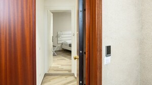 Un pasillo que conduce a un dormitorio con una cama, un tocador blanco y un interruptor de luz en la pared.