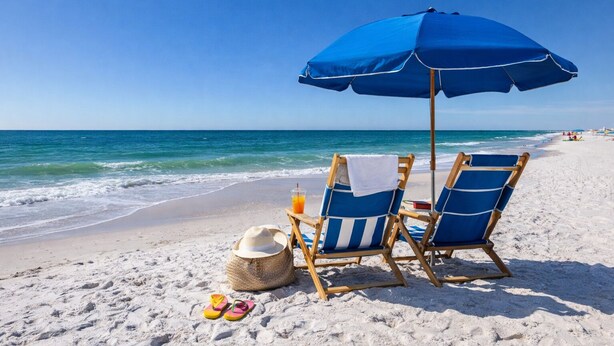 A beach scene with two blue beach chairs under a blue umbrella, a straw hat, and a pair of flip-flops on the sand. - Oceanfront | Heated Pools + Hot Tub | King | W/D | Cable (Orange Beach)