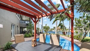 Ein Poolbereich mit Tisch und Stühlen, einer Pergola und Blick auf den Pool und Palmen.