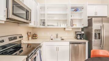 A modern kitchen with white cabinets, a stainless steel refrigerator, a built-in oven, and a coffee maker.
