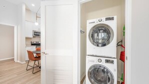 Un lavadero pequeño con dos lavadoras apiladas, un comedor con una silla y una cocina con microondas.