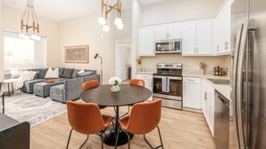 Una cocina moderna con armarios blancos, electrodomésticos de acero inoxidable y una zona de comedor con una mesa redonda y sillas naranjas.