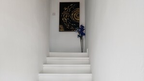 Una escalera blanca que lleva a una plataforma con un aplique de luz y una obra de arte enmarcada.