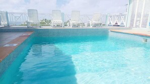 Una piscina con agua azul cristalina, rodeada de sillas de descanso blancas y una cerca blanca.