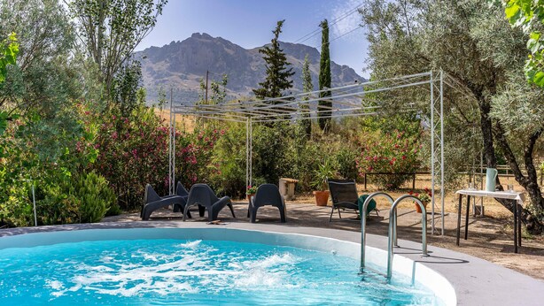 A swimming pool with a mountain backdrop, surrounded by greenery and outdoor seating.