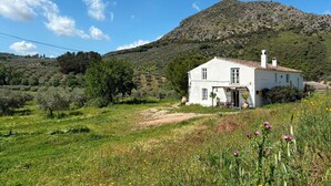 A white house with a tiled roof, surrounded by a grassy field and a mountain in the background.